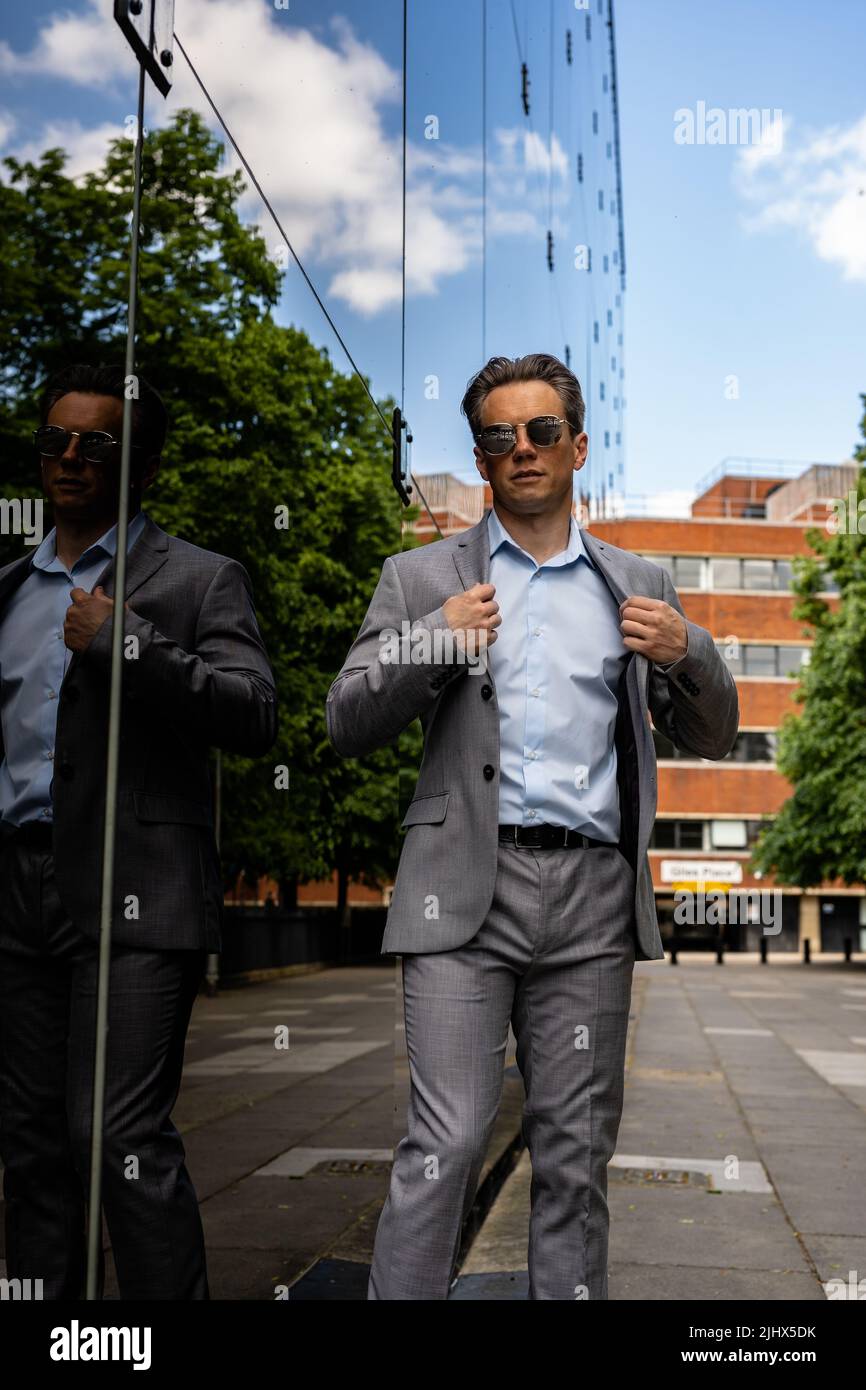 Un beau homme d'affaires dans un costume gris et des lunettes de soleil dans un environnement urbain Banque D'Images