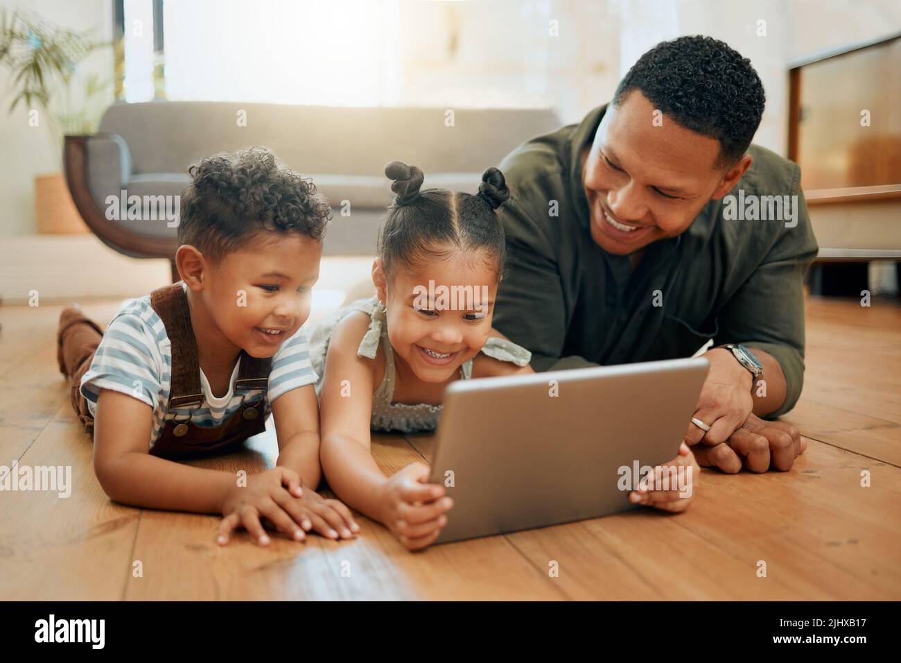 Une famille de trois personnes de race mixte se détendant et se couchée au rez-de-chaussée ensemble. Aimant noir parent unique liant avec ses enfants tout en utilisant un Banque D'Images