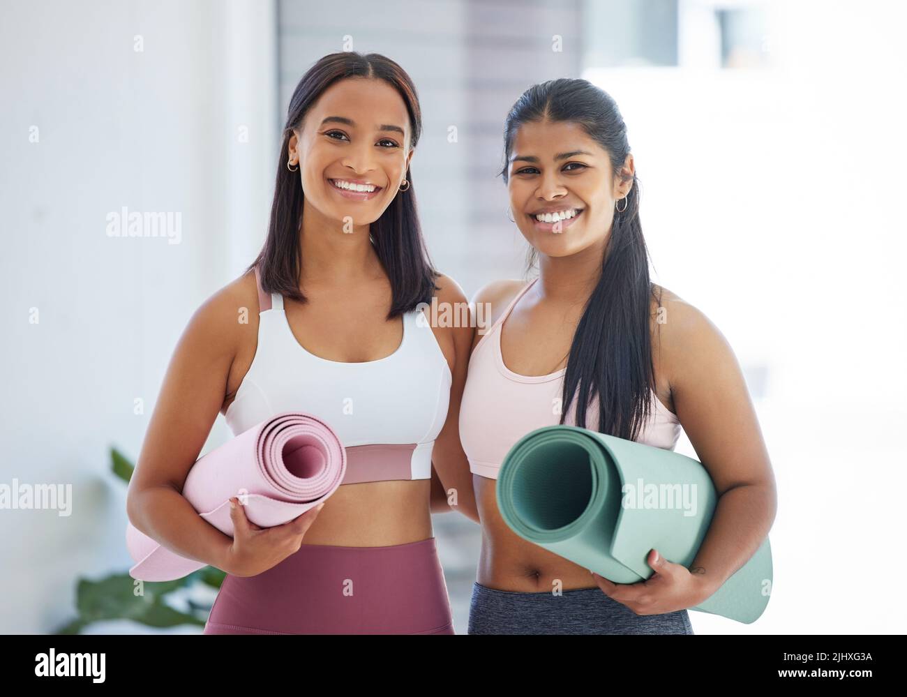 Rejoindre ces cours a été la meilleure décision jamais prise. Portrait de deux jeunes femmes sportives tenant des tapis d'exercice dans un studio de yoga. Banque D'Images