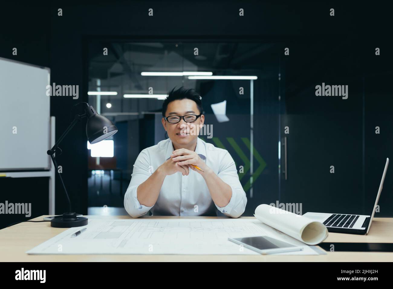 Portrait d'un architecte asiatique réussi souriant et regardant l'appareil photo, travaillant sur le plan de projet dessinant dans le bureau de studio de conception Banque D'Images
