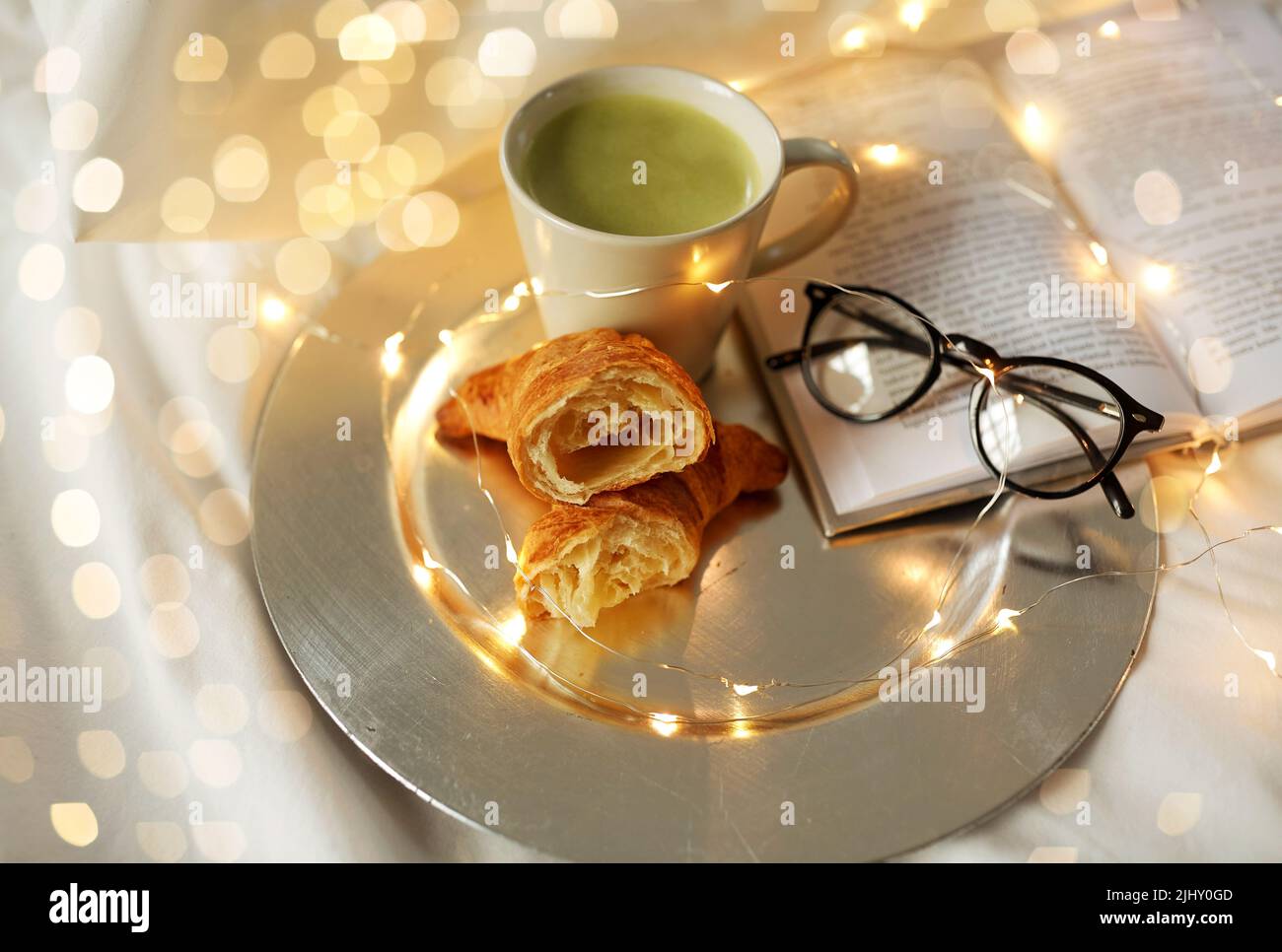 croissants, thé au matcha, livre et verres au lit Banque D'Images