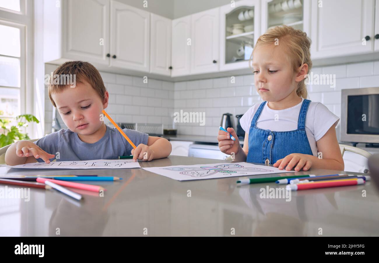 Jeunes frères et sœurs caucasiens de petite taille dessinant avec des crayons de couleur tout en étant assis au comptoir de la cuisine à la maison. Frère et sœur étant coloriage créatif Banque D'Images