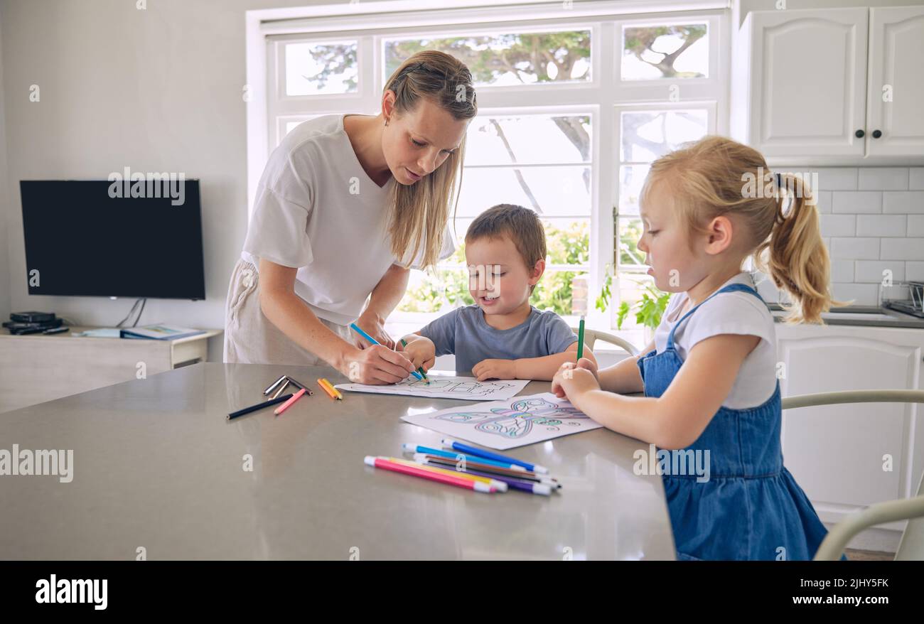 Jeune mère célibataire aidant ses deux petits enfants avec leurs devoirs dans une cuisine lumineuse. Deux frères et sœurs font leur projet scolaire Banque D'Images