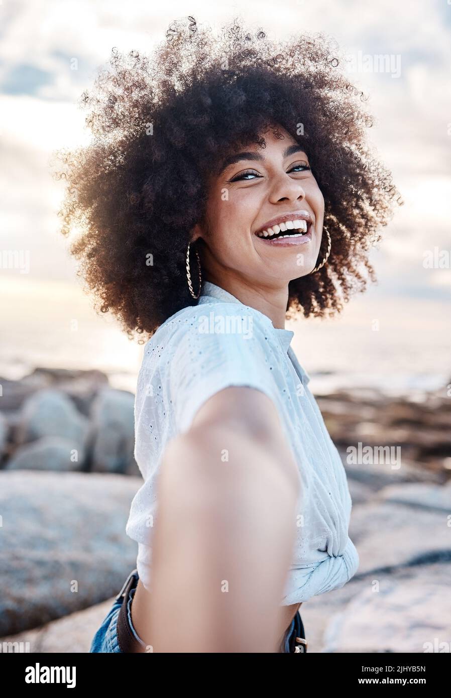 Une jeune femme de race mixte souriant sur la plage tout en atteignant sa main. Bonne femme hispanique avec une coiffure afro frais en plein air Banque D'Images