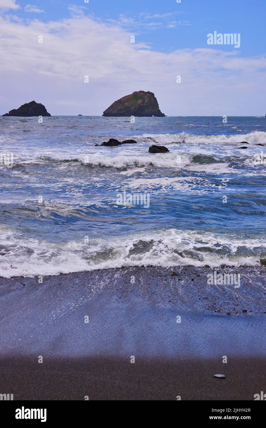 Vagues qui frappent la plage de sable noir sur la côte ouest Banque D'Images