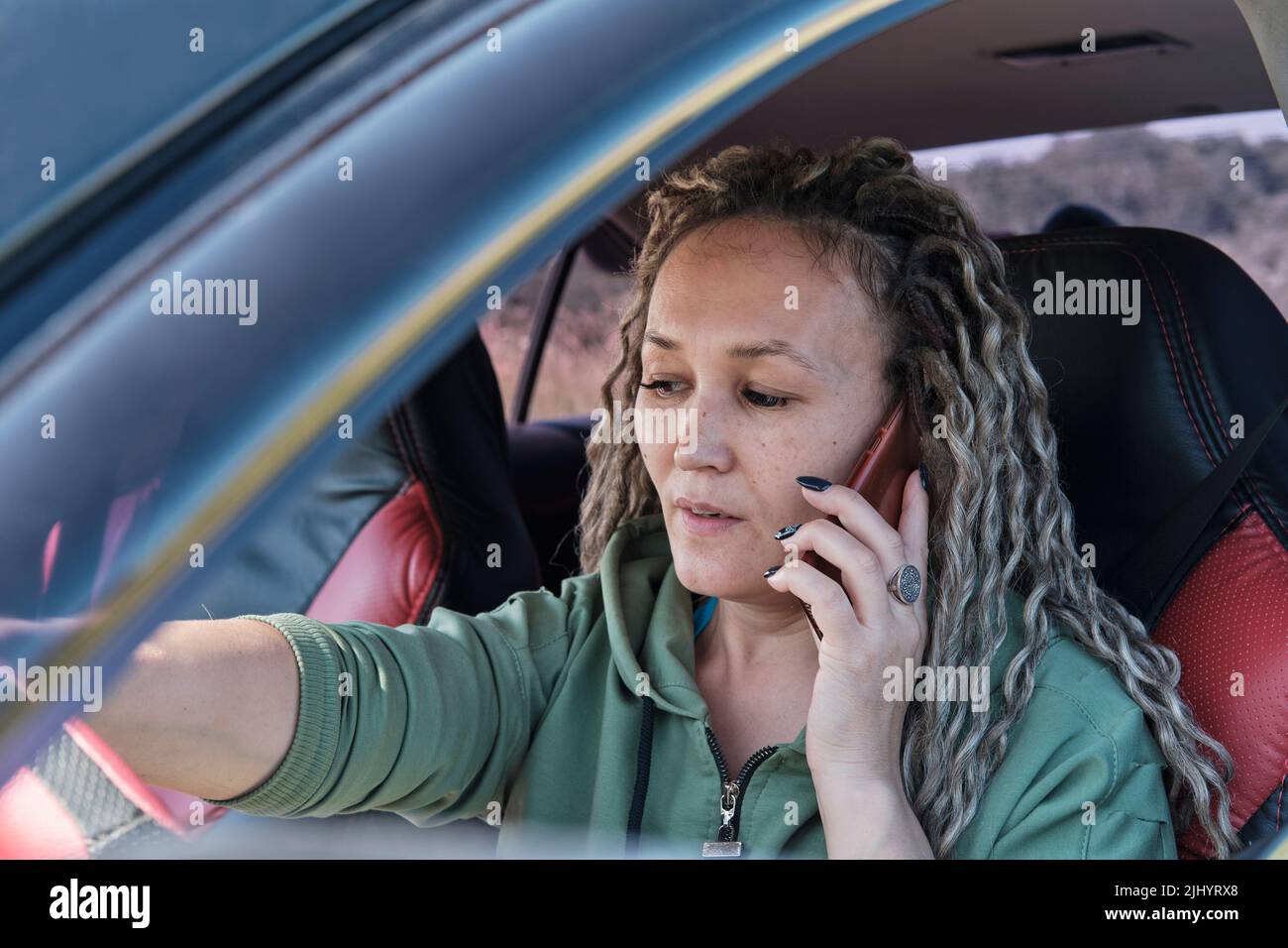 Belle femme asiatique d'âge moyen assise dans une voiture parlant au téléphone. Banque D'Images