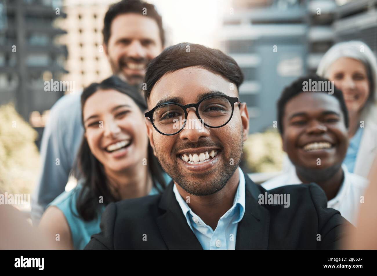 Dites fromage. Un beau jeune homme d'affaires debout à l'extérieur avec ses collègues et prenant des selfies. Banque D'Images