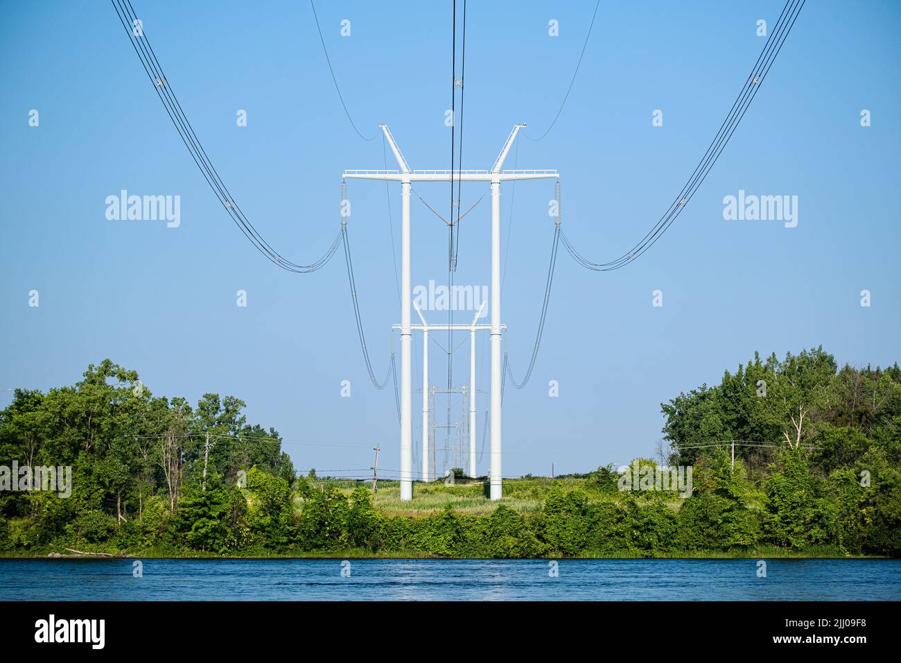 Colonnes de poteaux modernes de distribution d'énergie électrique avec des câbles traversant une rivière dans une région rurale. Banque D'Images