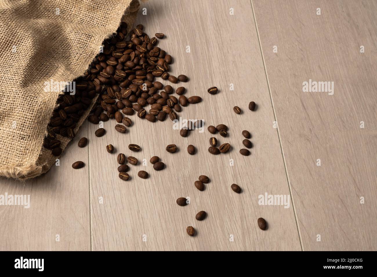 Des grains de café débordent d'un sac hessien sur un fond clair Banque D'Images