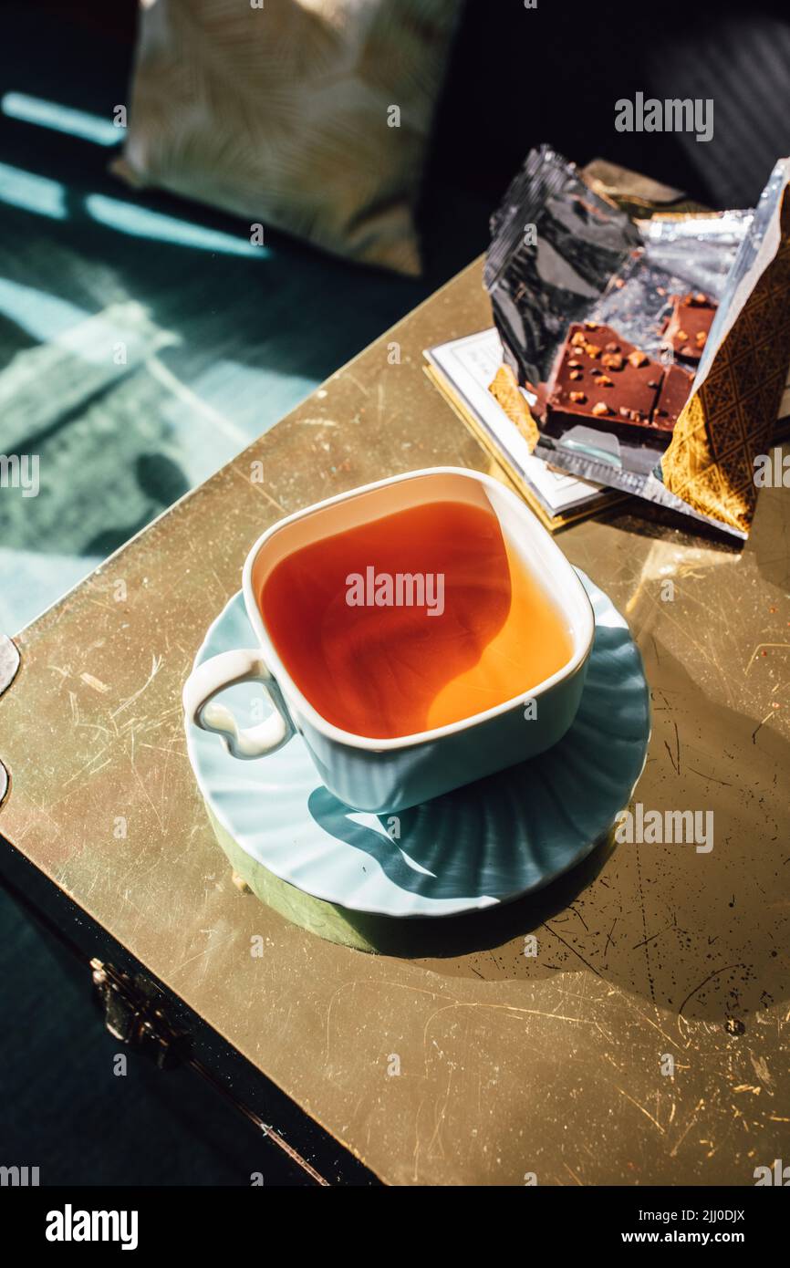 thé de l'après-midi dans la tasse carrée de thé et soucoupe avec chocolat dans l'emballage doré Banque D'Images