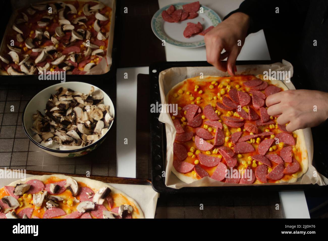 Permet de déconcentrer les ingrédients de la pizza sur la pâte. Homme en cuisine. Sauce tomate rouge, saucisses, maïs doux, champignons. Pizza maison. Base de Margarita. Accueil culina Banque D'Images