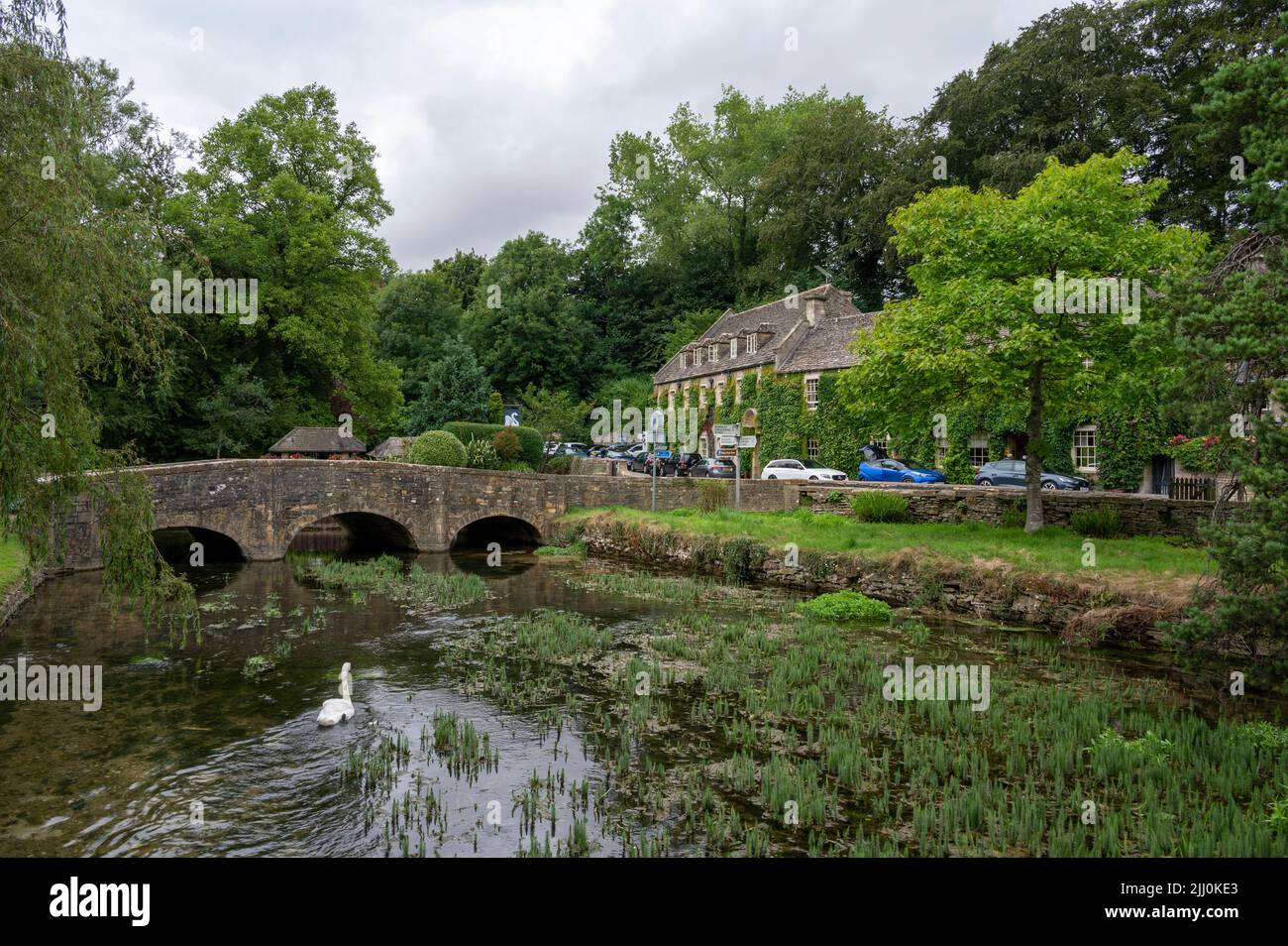 Un pont sur une rivière et un chalet en pierre entouré d'arbres verts dans le village de Bibury Banque D'Images