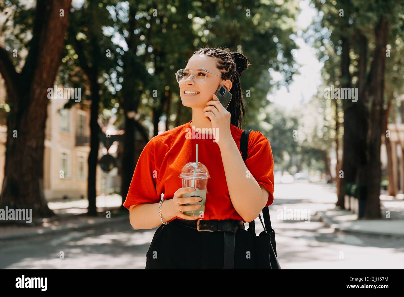 Une photo d'une jeune femme avec des tresses de boîte parlant à son téléphone tout en tenant une boisson Banque D'Images