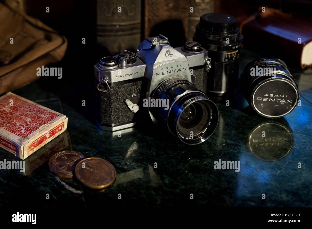 Un gros plan d'un appareil photo Pentax vintage avec objectif Asahi, livres, cartes à jouer et pièces de monnaie sur le comptoir Banque D'Images
