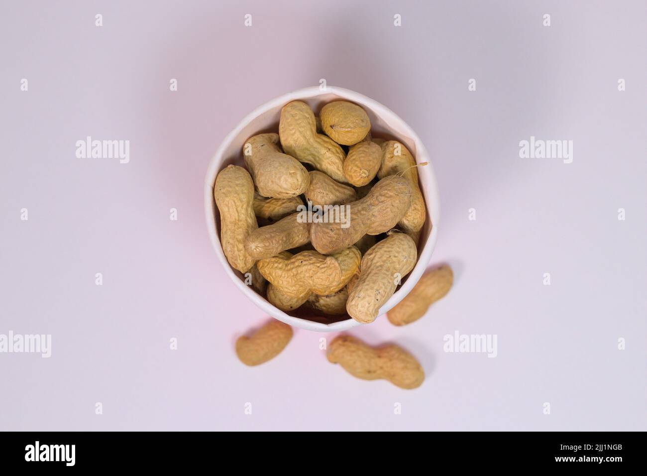 Décortiqueter les arachides dans une tasse en papier sur une surface blanche Banque D'Images