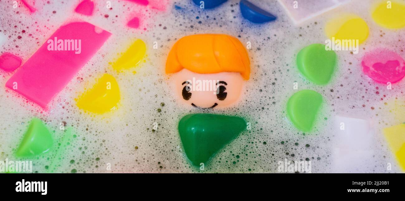 Le lavage de banderoles de jouets pour enfants, des blocs de construction en plastique avec des figurines. Un petit ami souriant et des cubes colorés flottent dans l'eau mousseuse. Banque D'Images