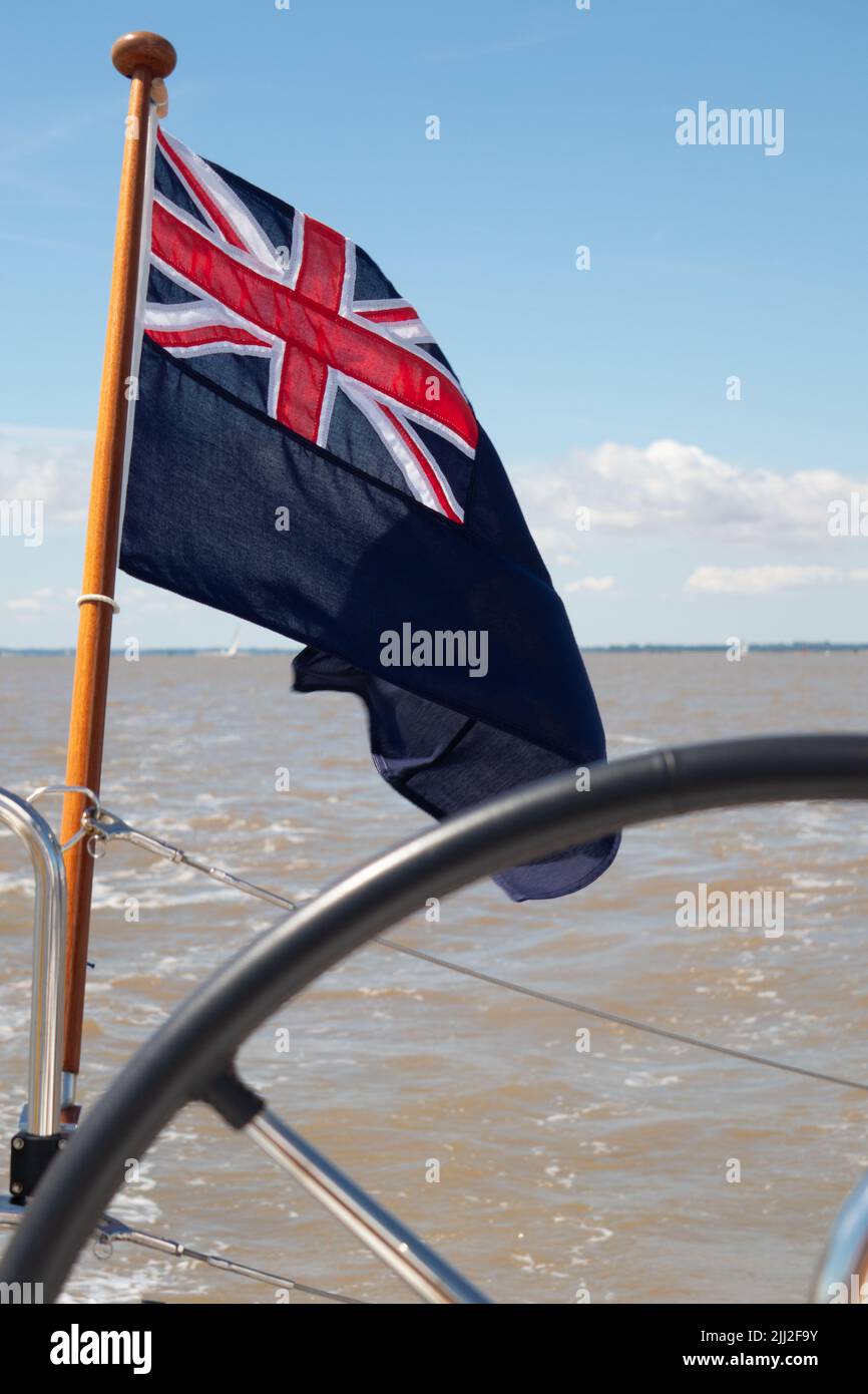 Blue Ensign sur un flagstaff en bois volant sur une poupe d'un yacht montrant une partie de la roue et de la mer en arrière-plan Banque D'Images