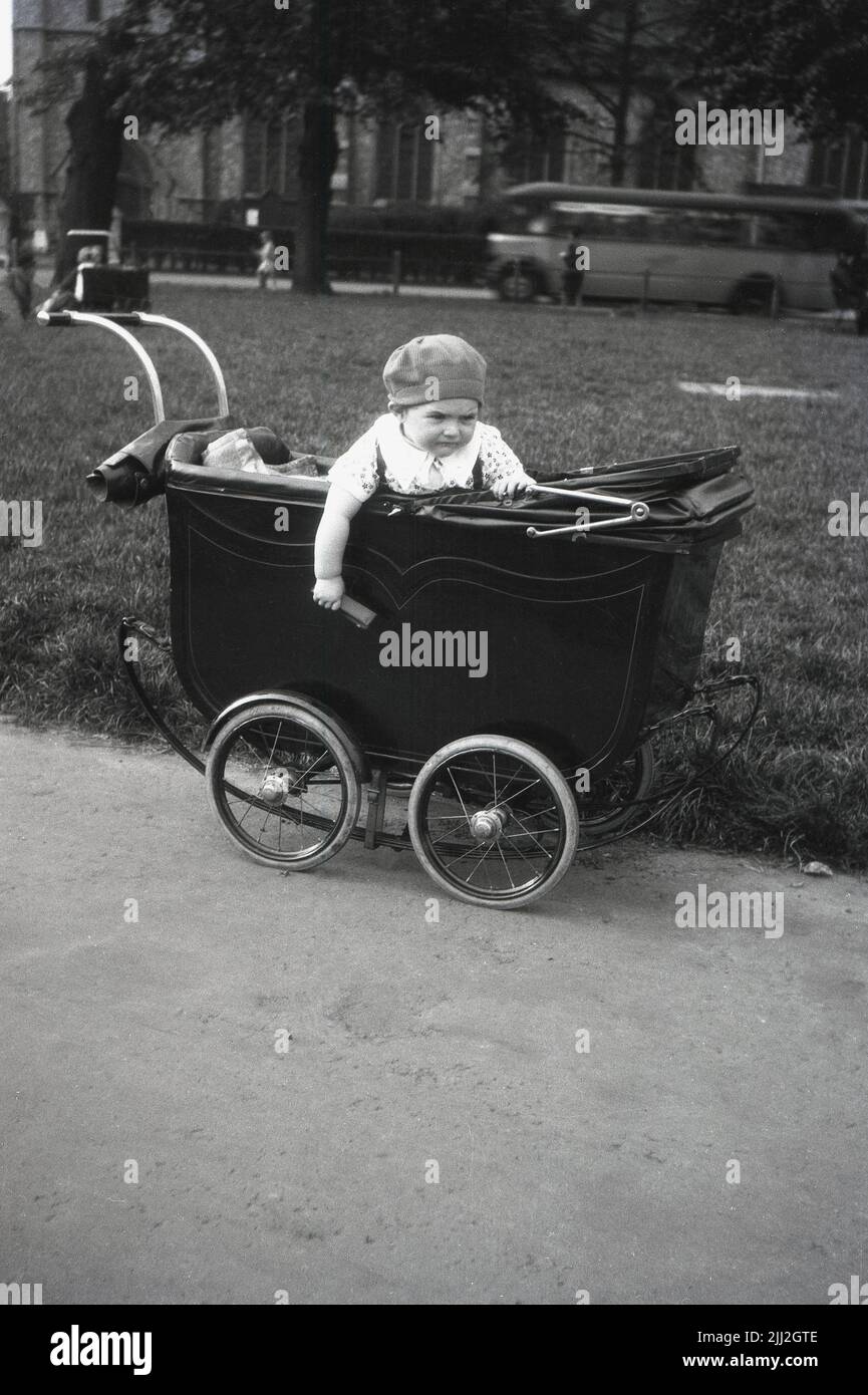 1940s, historique, à l'extérieur sur un chemin dans une banlieue de ville, un petit enfant avec le capot sur sa tête s'est assis dans un landau ou une poussette de l'époque, Angleterre, Royaume-Uni. Banque D'Images