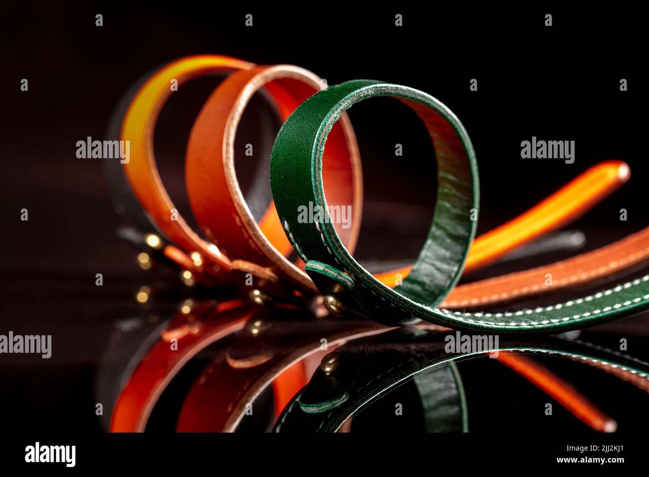 Un groupe de ceintures en cuir multicolores sur fond noir. Banque D'Images