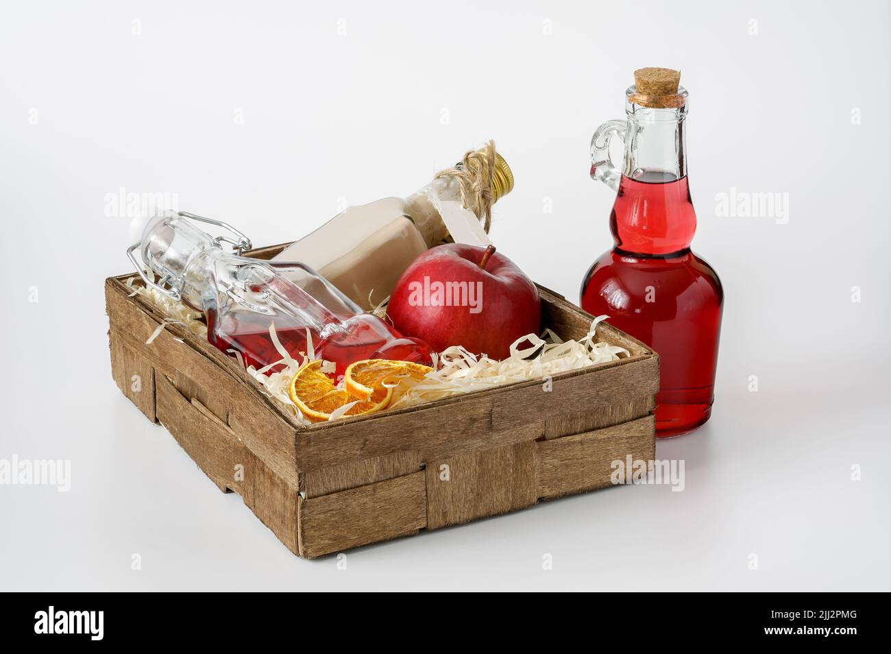 bouteilles de liqueurs dans une petite boîte décorative bordée de copeaux sur fond blanc, d'une pomme rouge et de tranches d'orange séchées Banque D'Images