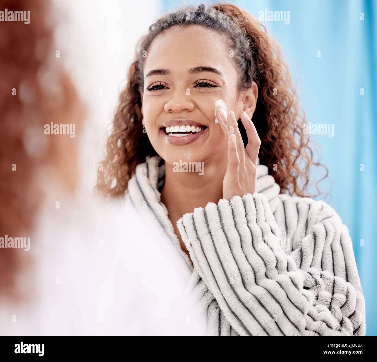 Donnez un peu d'amour à votre visage. Une jeune femme attrayante appliquant de la lotion sur son visage dans la salle de bains à la maison. Banque D'Images