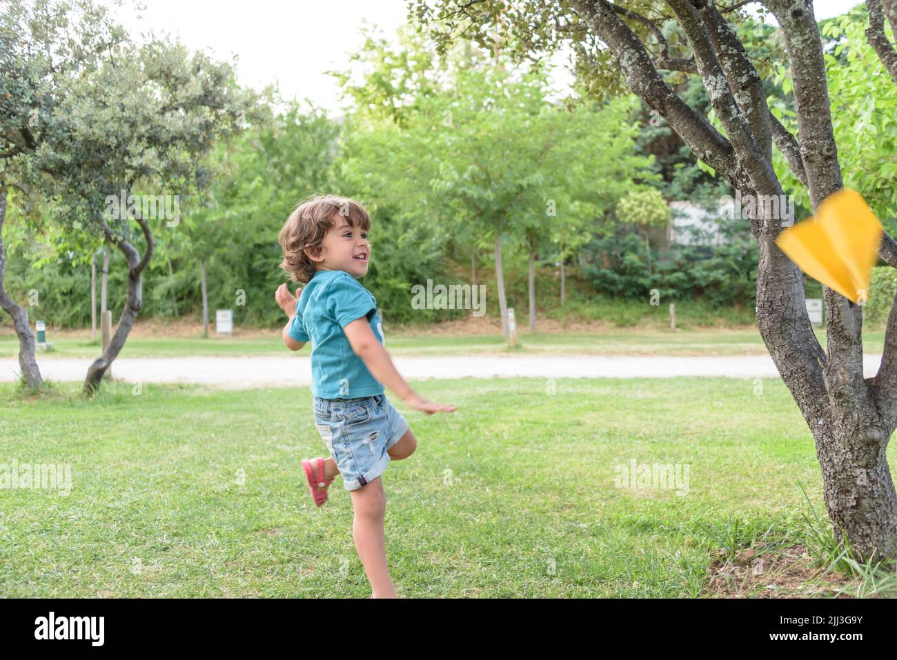 Garçon jouant à jeter un avion de papier à l'extérieur en regardant loin. Portrait d'un garçon caucasien gai jouant dans le parc de printemps et d'été ayant du plaisir sur le Banque D'Images
