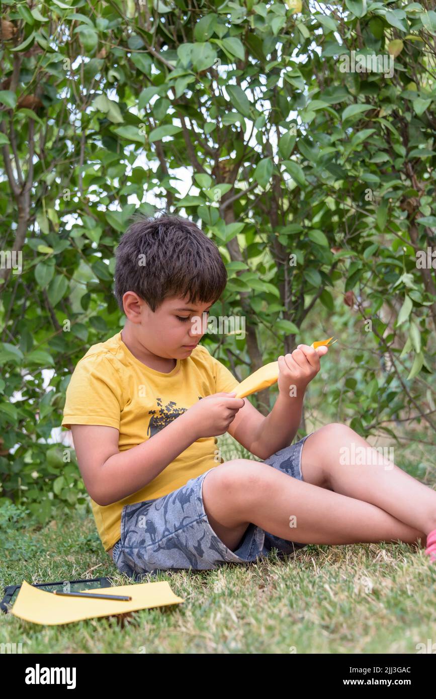 Garçon jouant à jeter un avion de papier à l'extérieur en regardant loin. Portrait d'un garçon caucasien gai jouant dans le parc de printemps et d'été ayant du plaisir sur le Banque D'Images