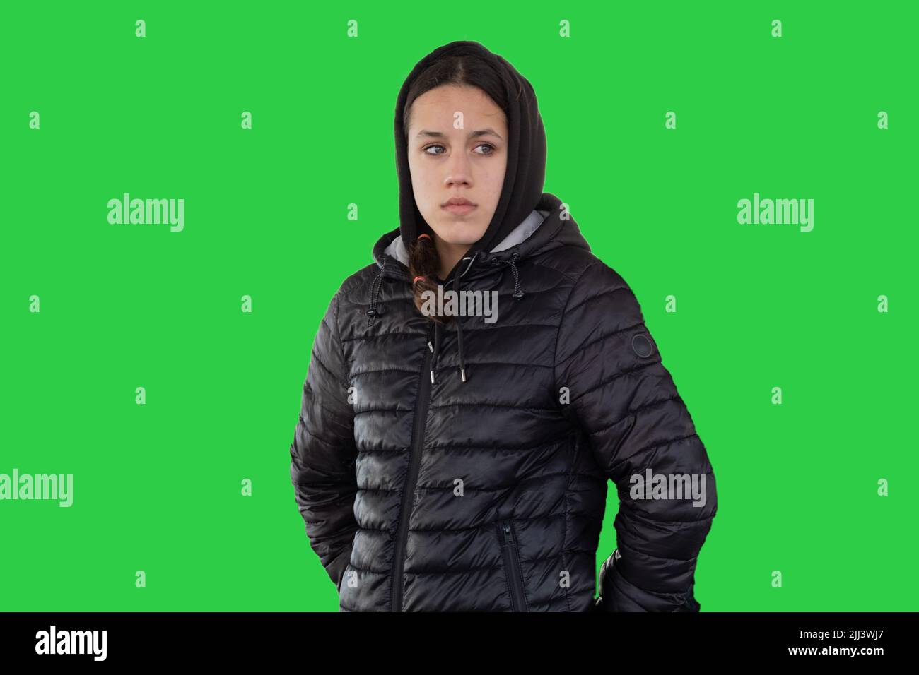 Une adolescente porte une veste à capuche noire en duvet et regarde loin. Une expression du visage triste ou inquiète. Fond vert, couleur verte psychologie: envy. Banque D'Images