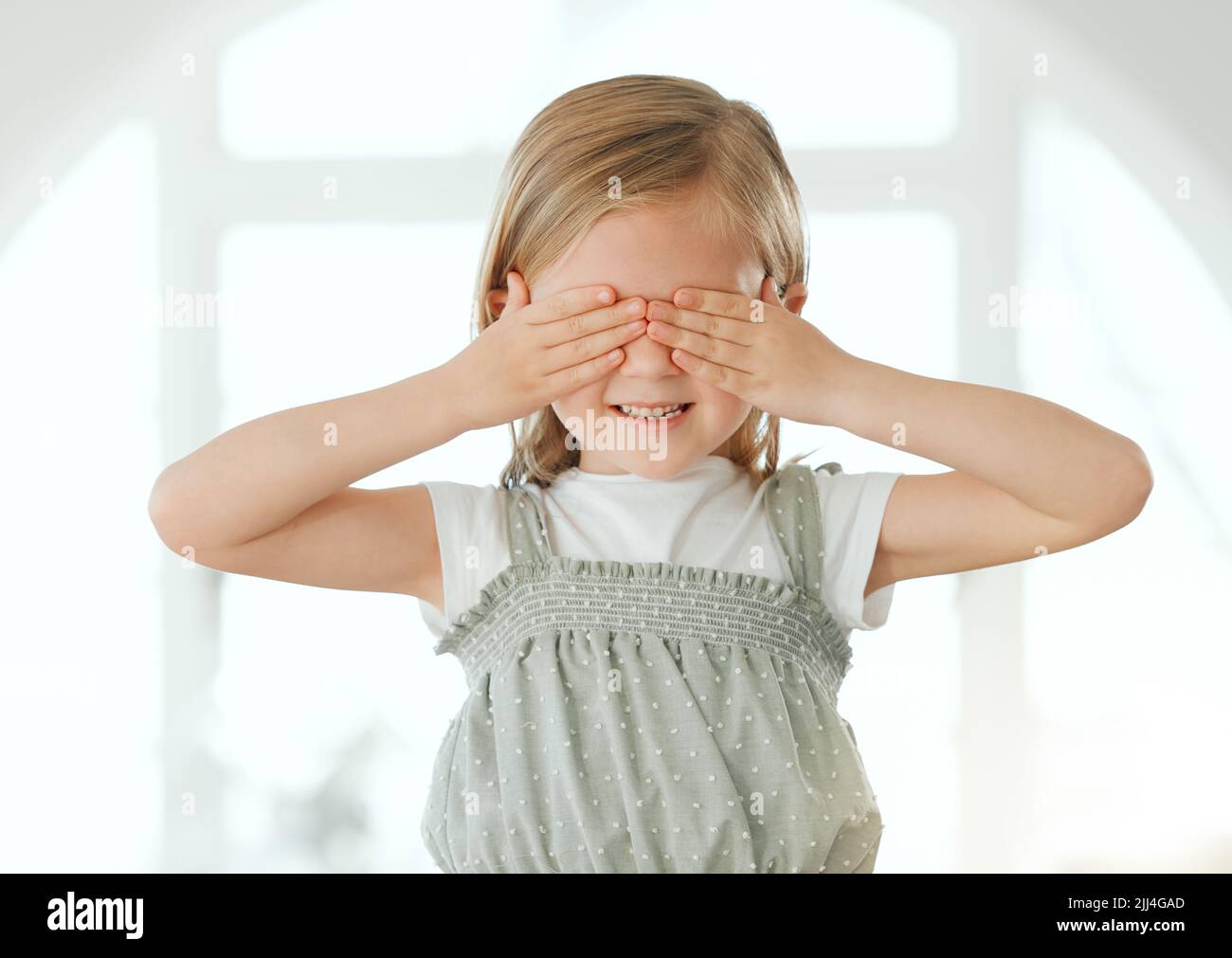 Je ne veux pas regarder. Une adorable petite fille debout seule à la maison et couvrant ses yeux avec ses mains. Banque D'Images
