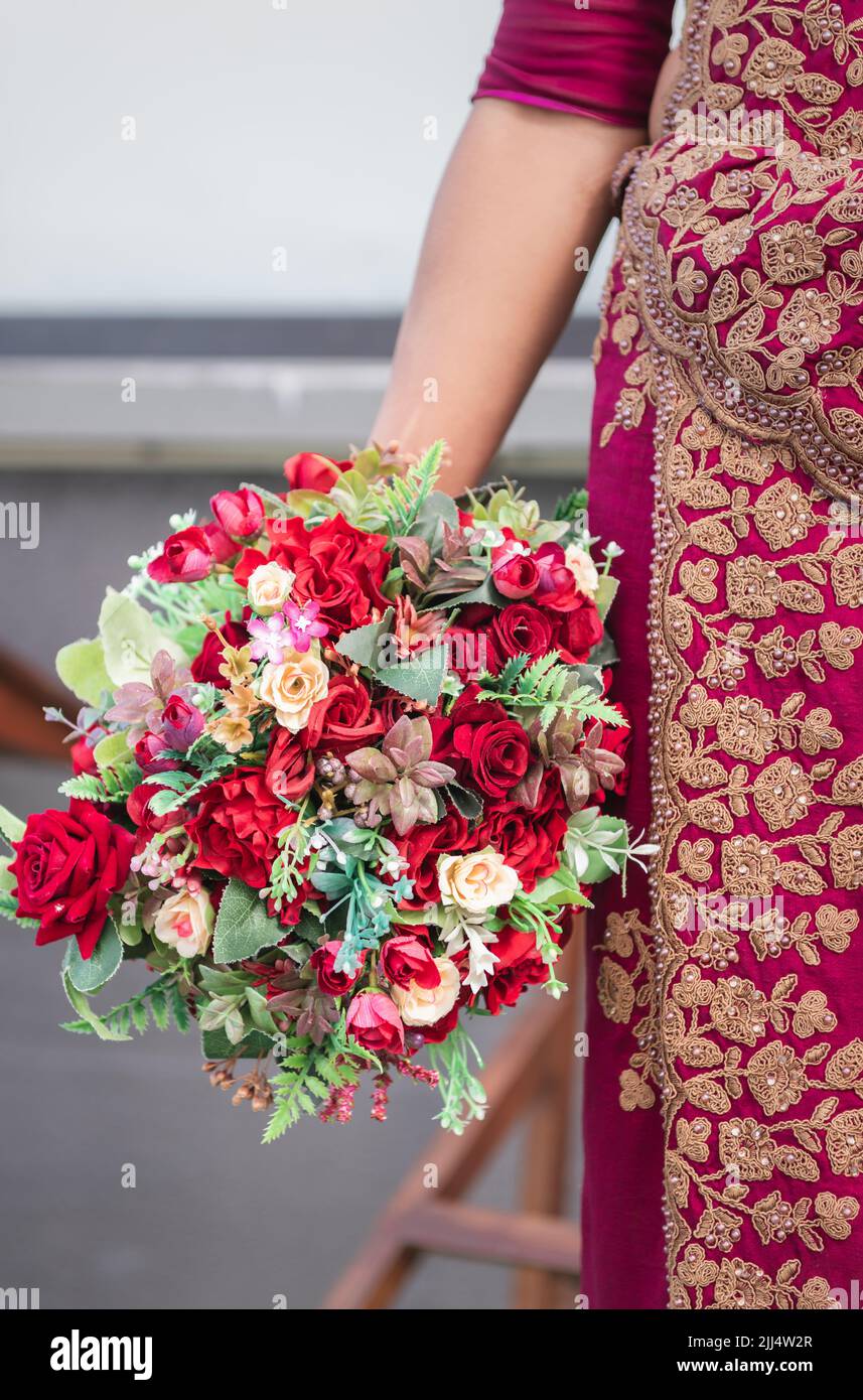 Mariée tenant bouquet de fleurs photo en gros plan, belle mariée rouge habillée de retour avec beaucoup de bijoux d'or. Concept du jour le plus heureux de la vie. Banque D'Images