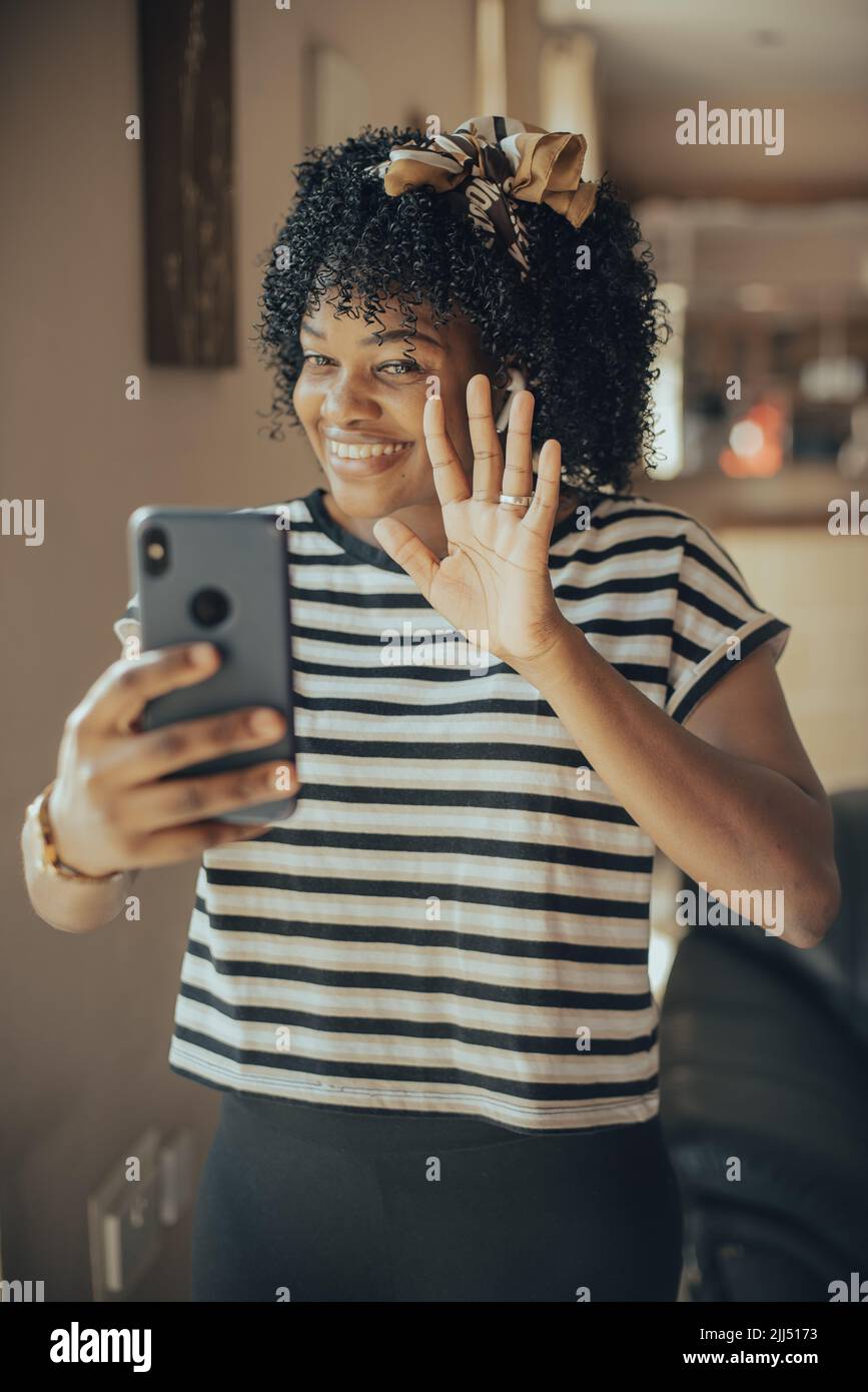 Jeune femme portant un t-shirt rayé, femme souriante tenant un smartphone avec des écouteurs à l'intérieur Banque D'Images