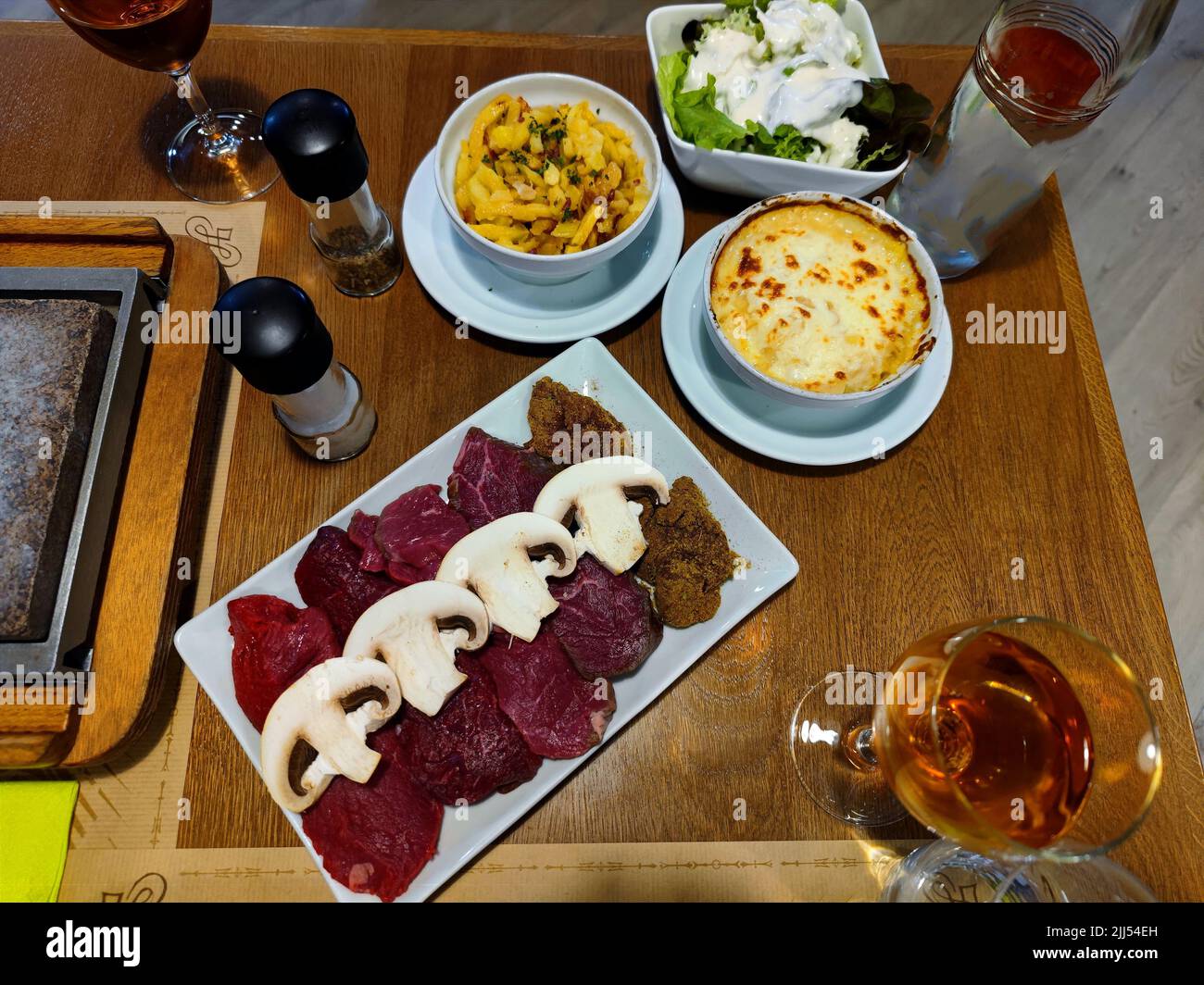 Délicieux différents types de steak avec des champignons et gratin de pommes de terre à côté sont sur un plat et prêt à être grillé sur un grill en pierre Banque D'Images