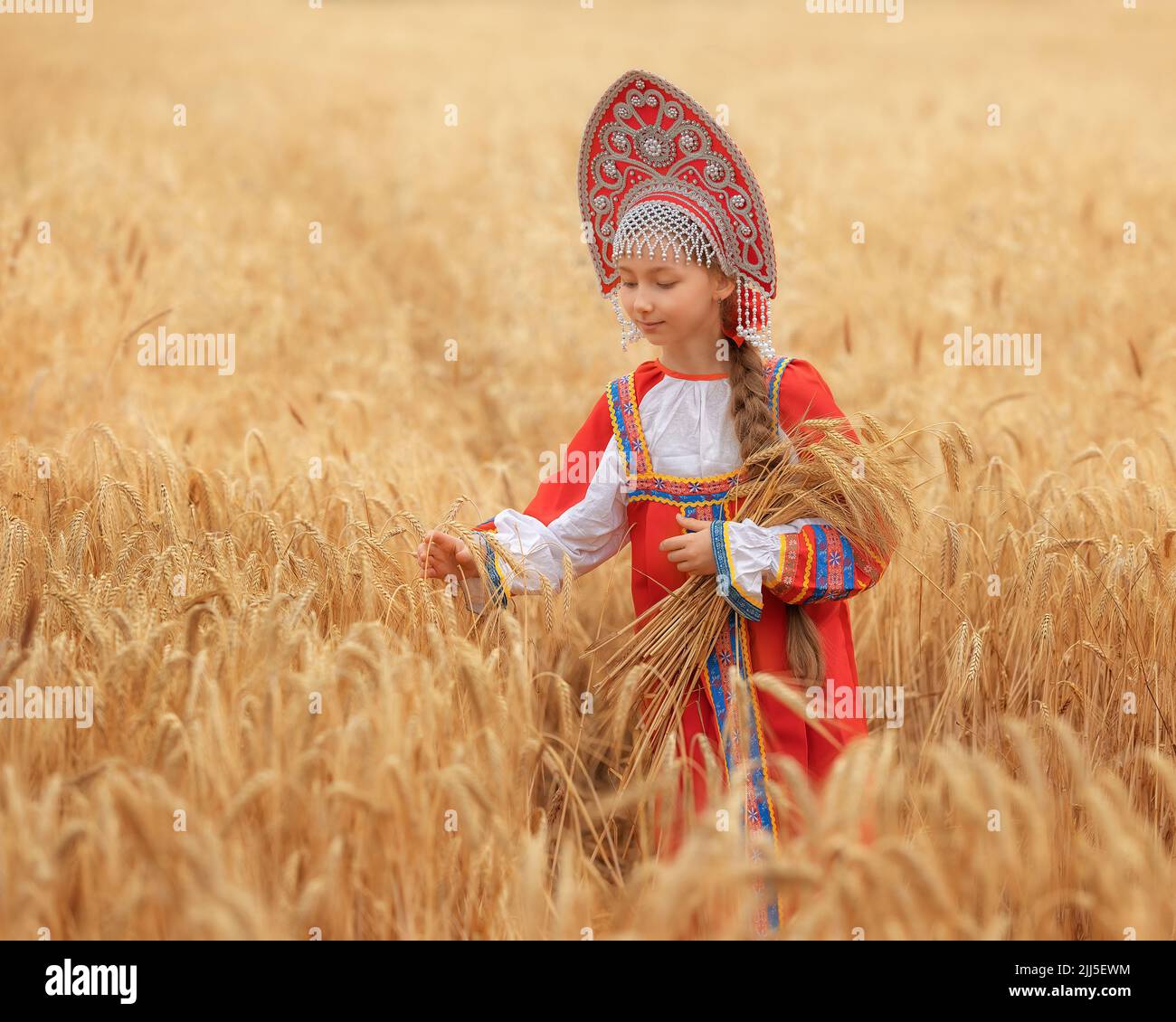 Littl petite fille dans le sarafan national russe et un kokoshnik debout dans un champ de blé doré en été Banque D'Images