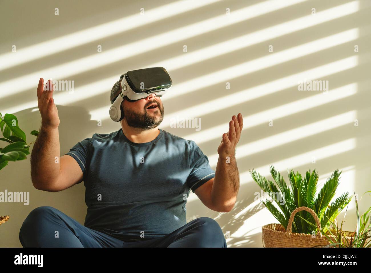 Homme joyeux portant des lunettes VR et faisant des gestes devant le mur Banque D'Images