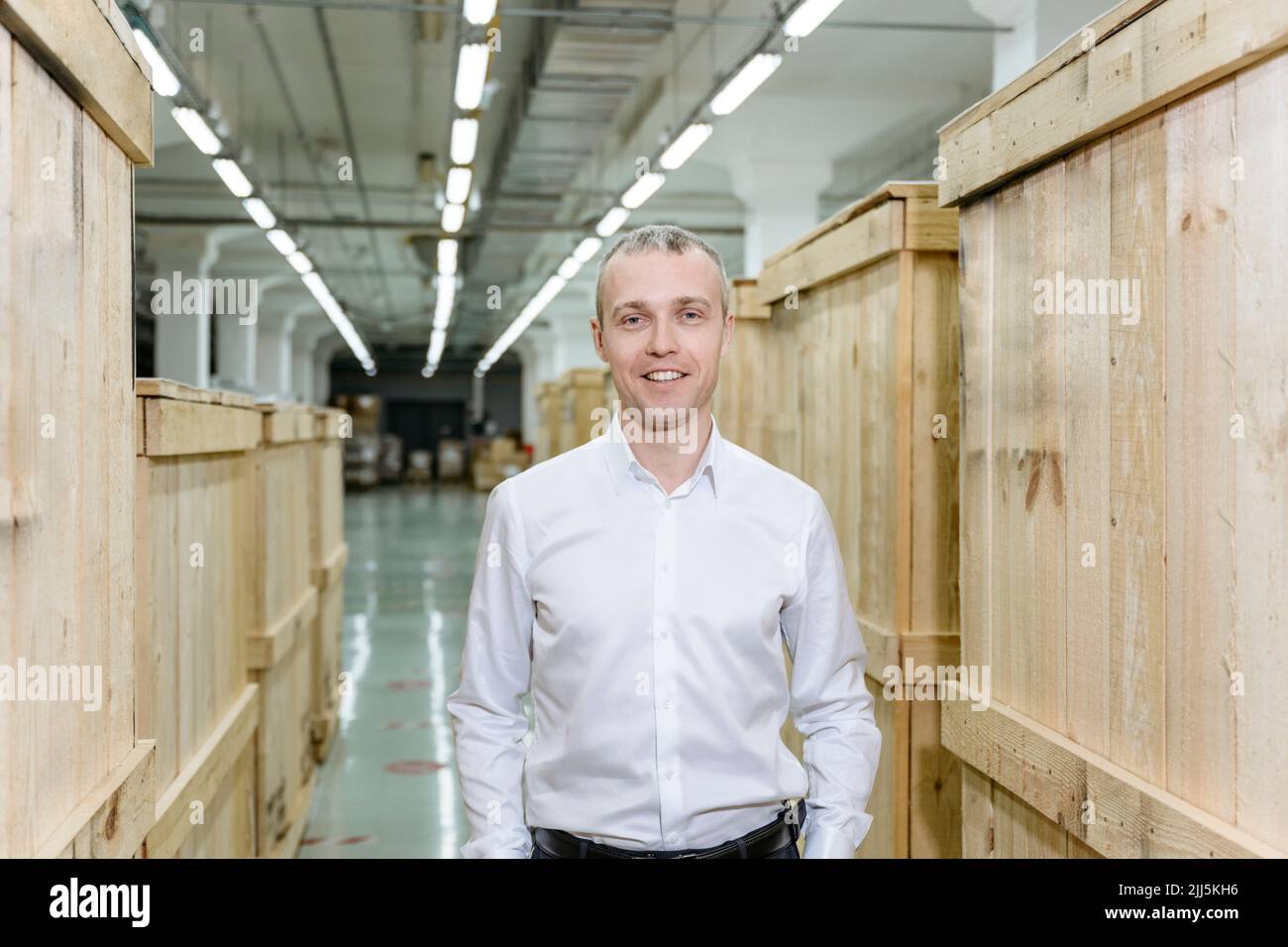 Homme d'affaires souriant debout au milieu de caisses en bois dans l'entrepôt Banque D'Images