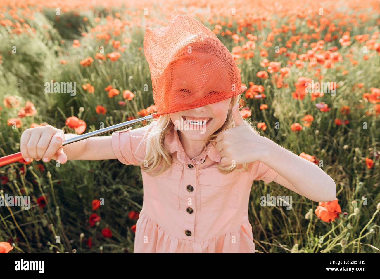 Fille joueur jouant avec le filet de papillon rouge dans le champ de pavot Banque D'Images
