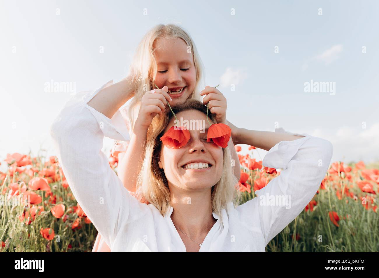 Une fille heureuse cachant les yeux de sa mère avec des fleurs dans le champ de pavot Banque D'Images