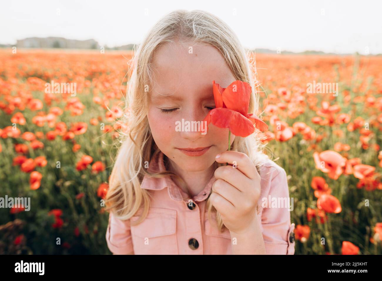 Fille couvrant l'œil avec fleur rouge dans le champ Banque D'Images