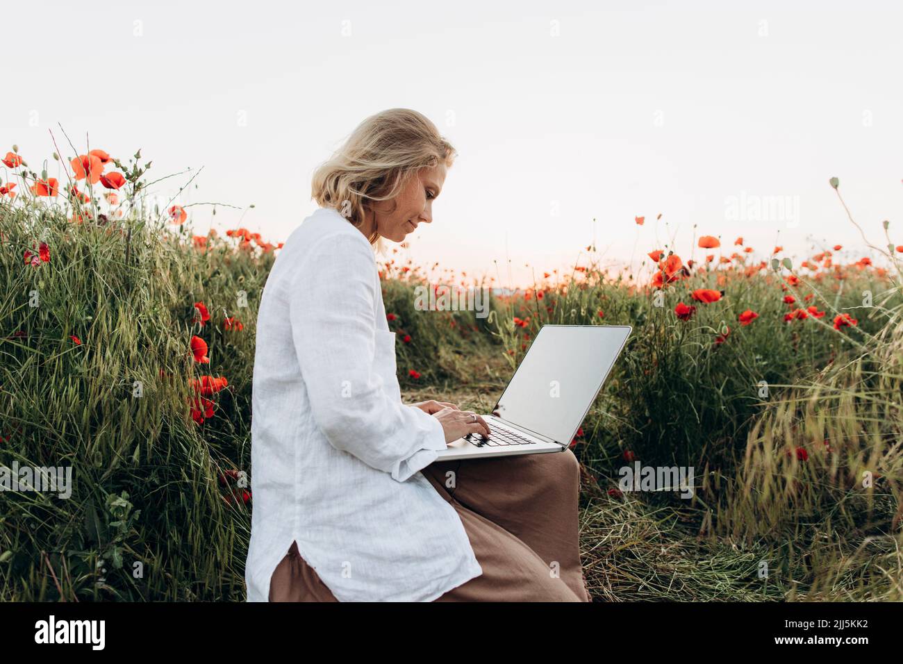 Femme souriante utilisant un ordinateur portable dans un champ de pavot Banque D'Images
