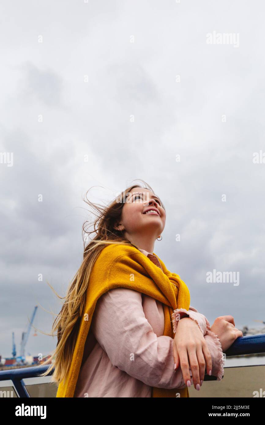 Jeune femme souriante debout sous un ciel nuageux Banque D'Images