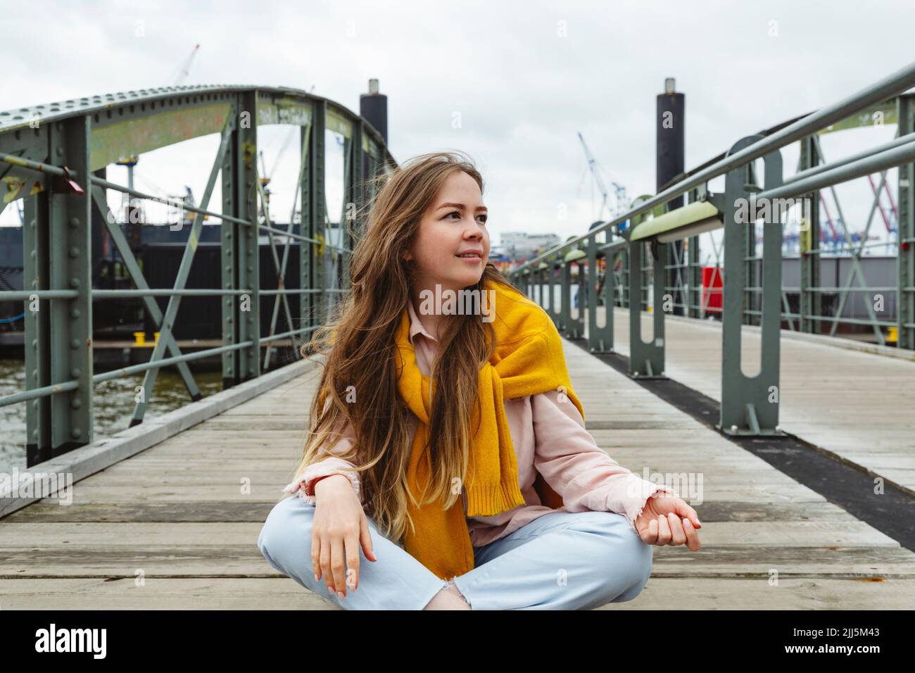 Jeune femme souriante avec de longs cheveux bruns assis sur la passerelle Banque D'Images
