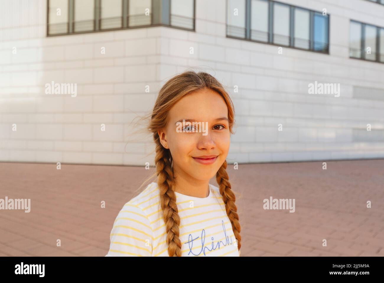Fille souriante avec cheveux tressés debout devant le bâtiment Banque D'Images