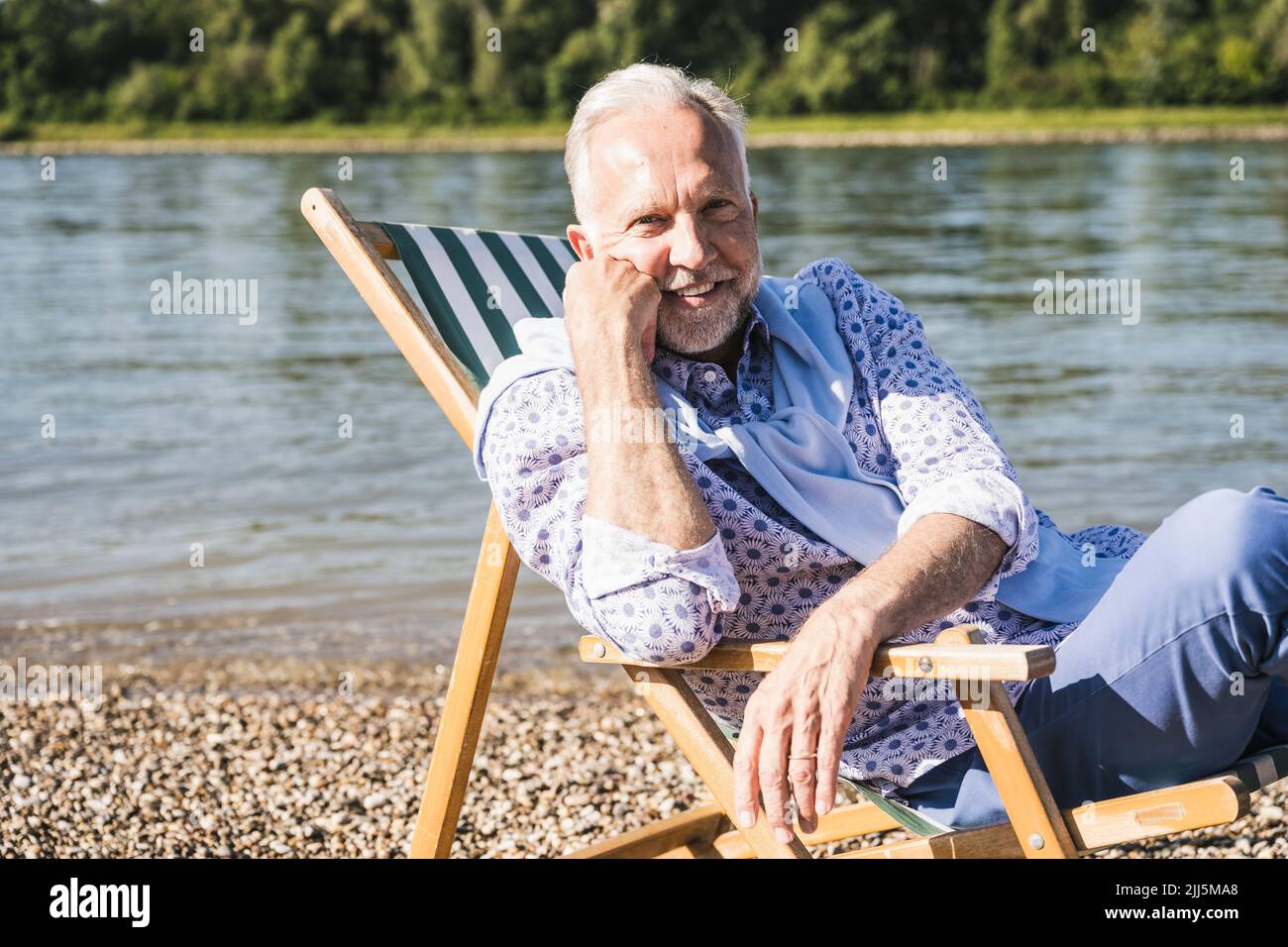 Homme âgé souriant et retraité assis sur une chaise longue au bord de la rivière Banque D'Images