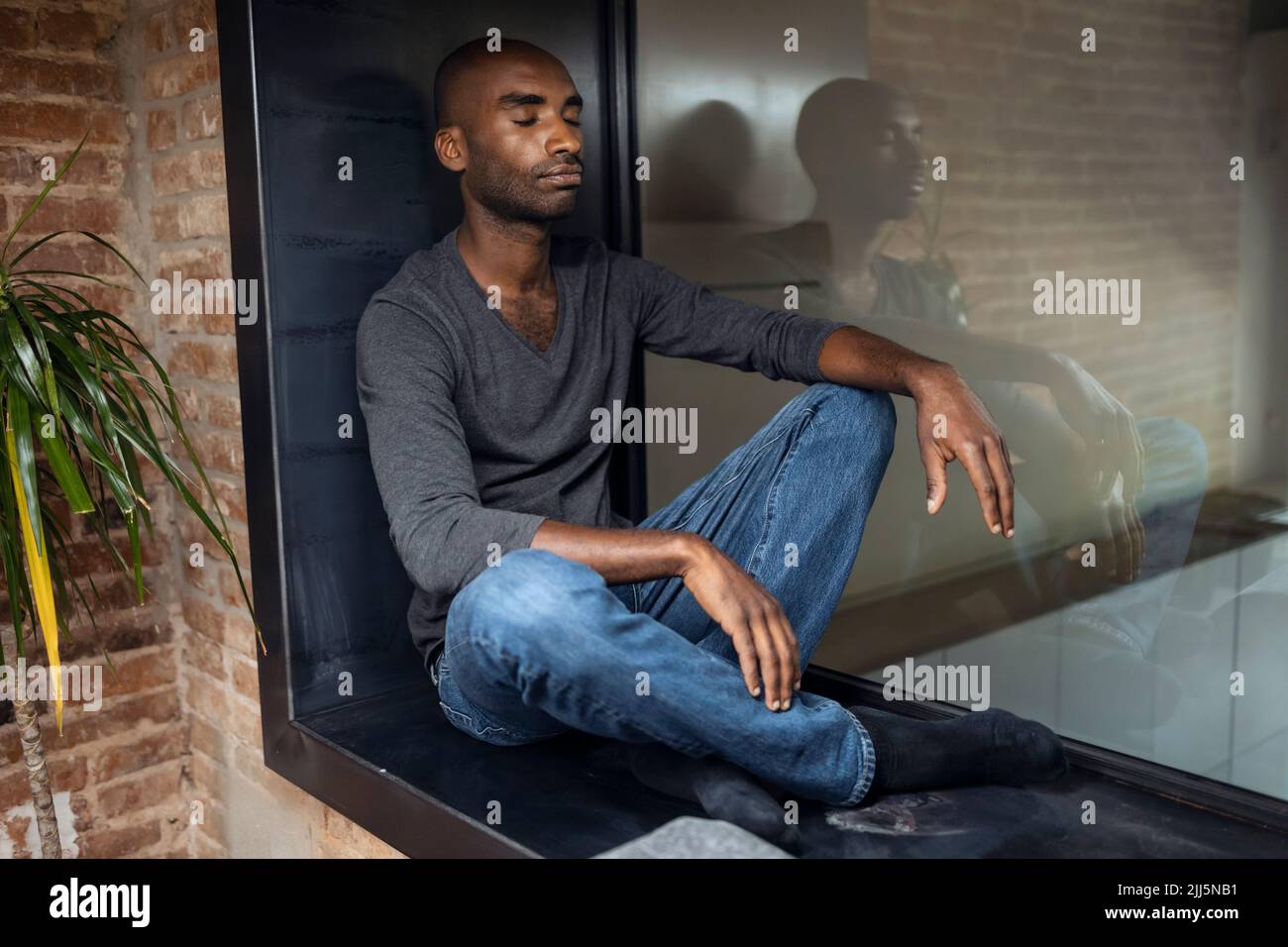 Chauve homme avec les yeux fermés assis sur le rebord de la fenêtre à la maison Banque D'Images