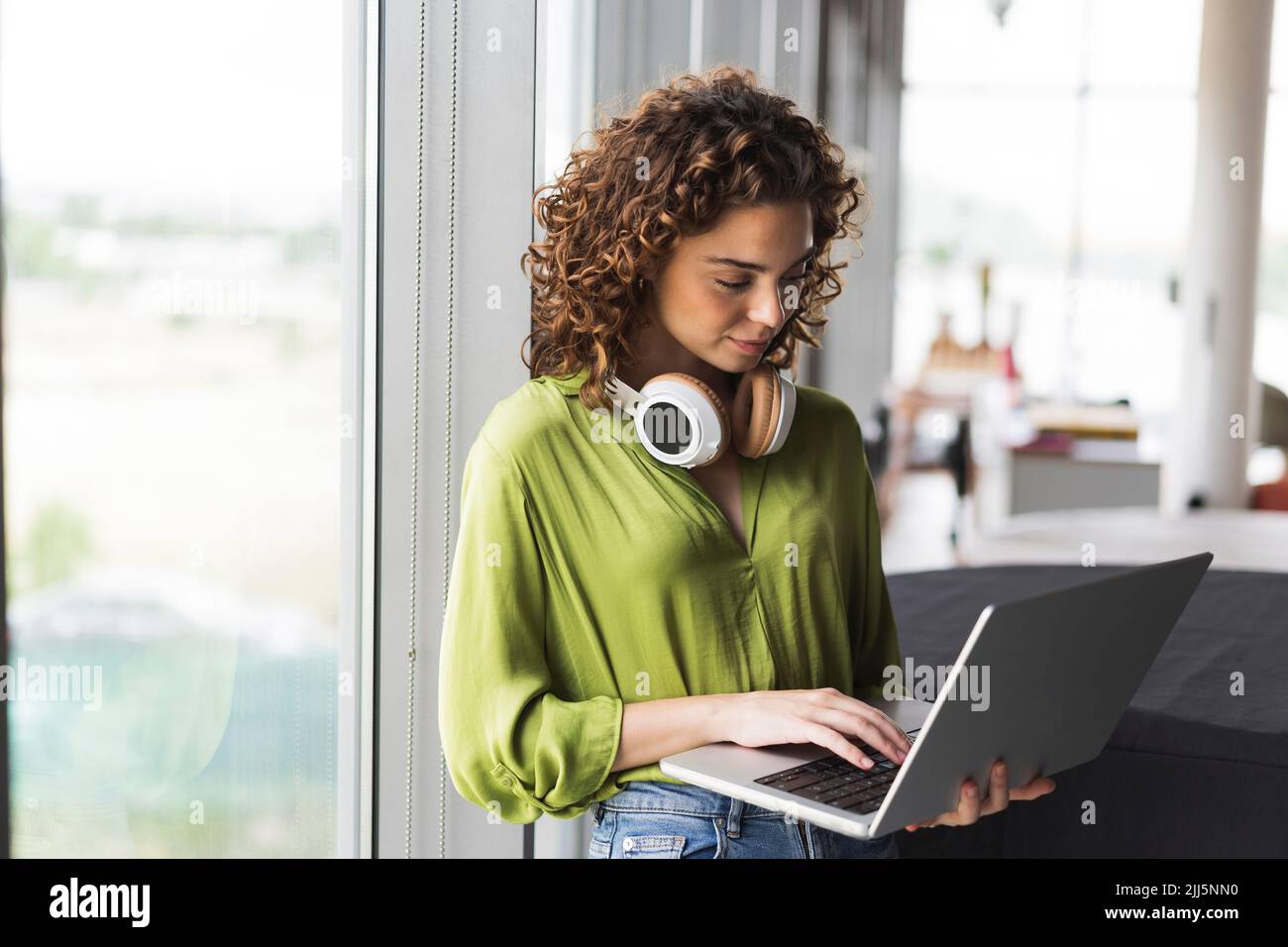 Femme d'affaires avec casque utilisant un ordinateur portable près de la fenêtre au bureau Banque D'Images