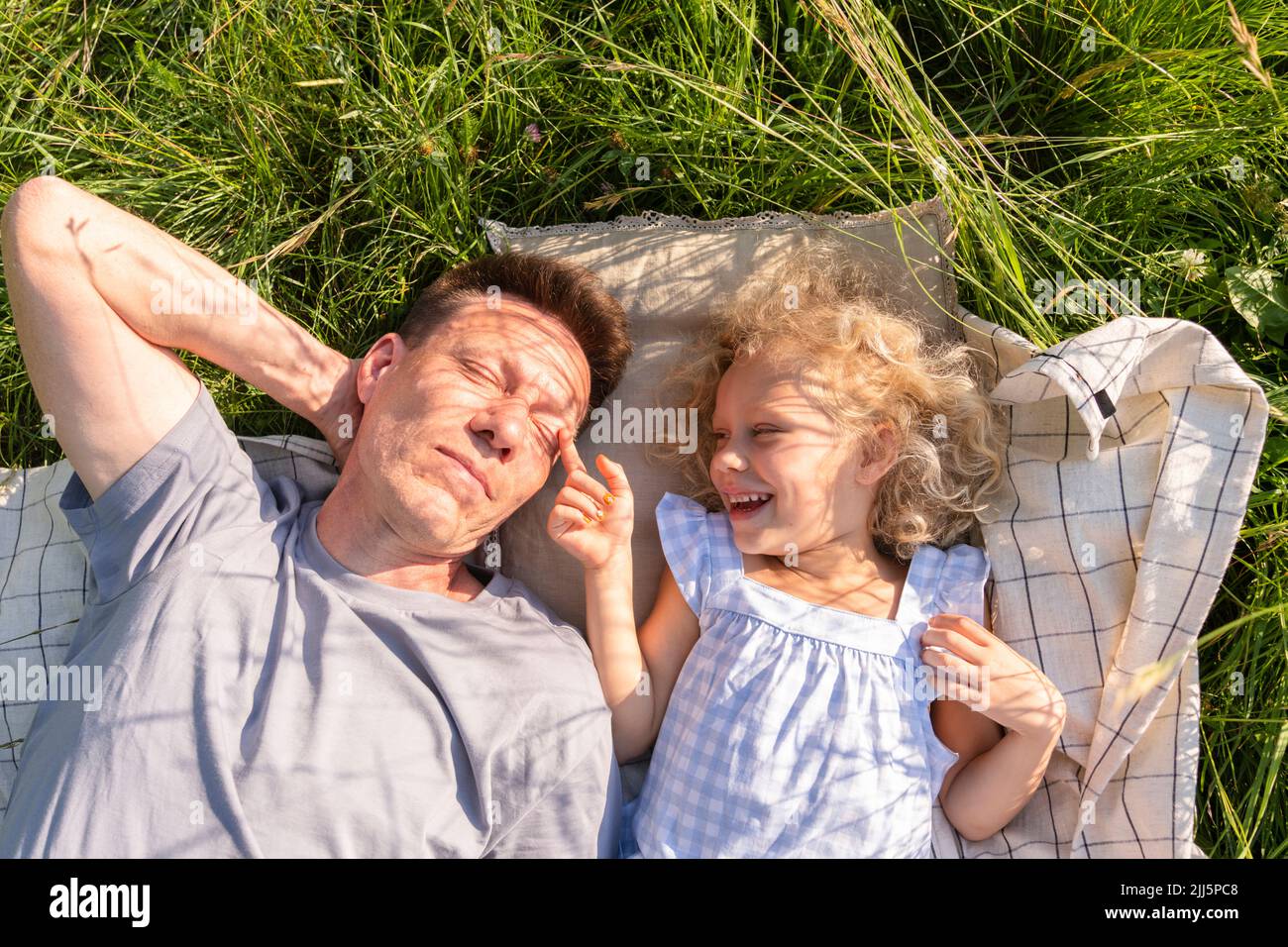 Bonne fille couchée avec son père sur une couverture de pique-nique au milieu de l'herbe Banque D'Images