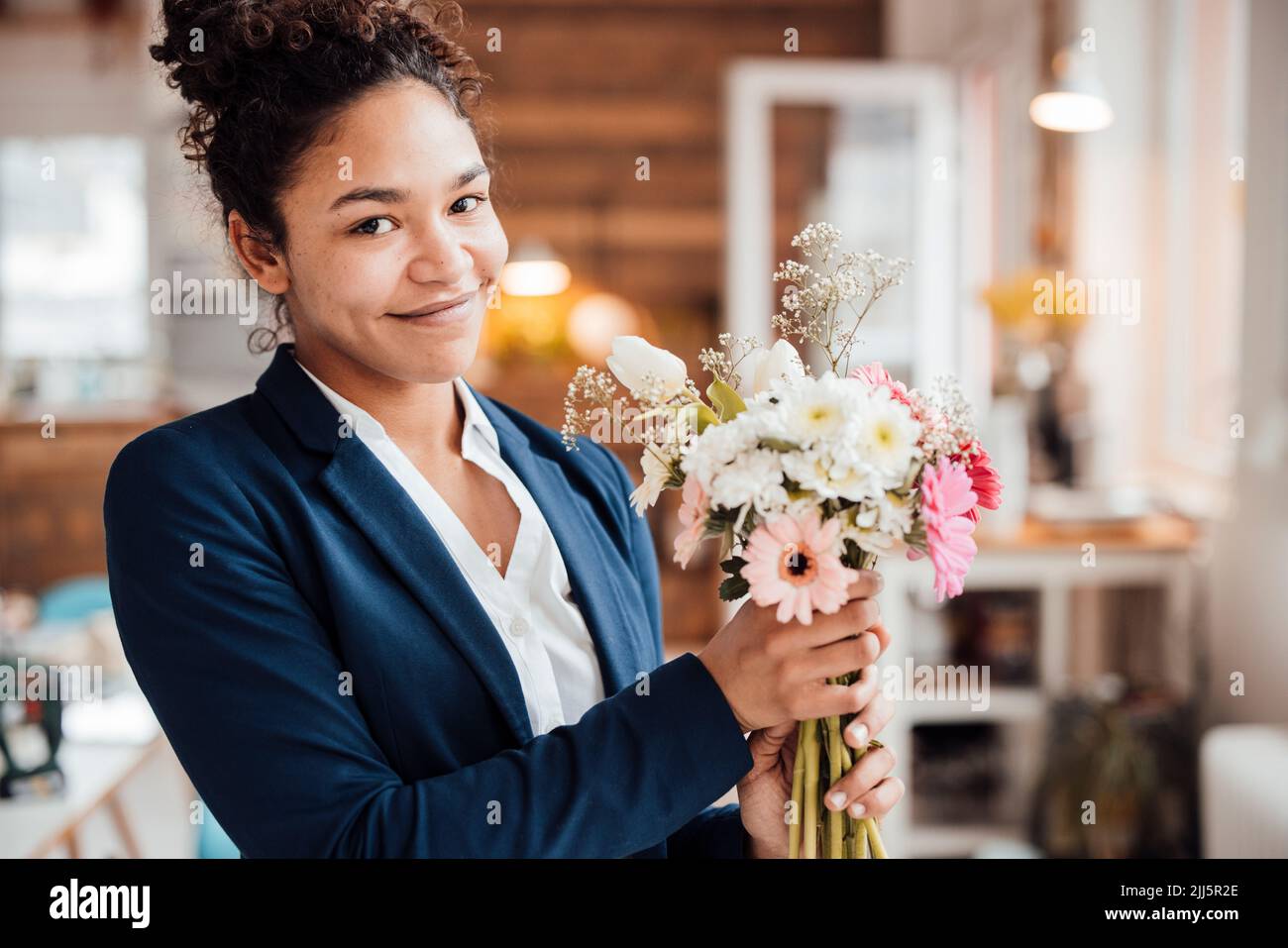 Jeune femme d'affaires souriante avec fleurs au bureau Banque D'Images