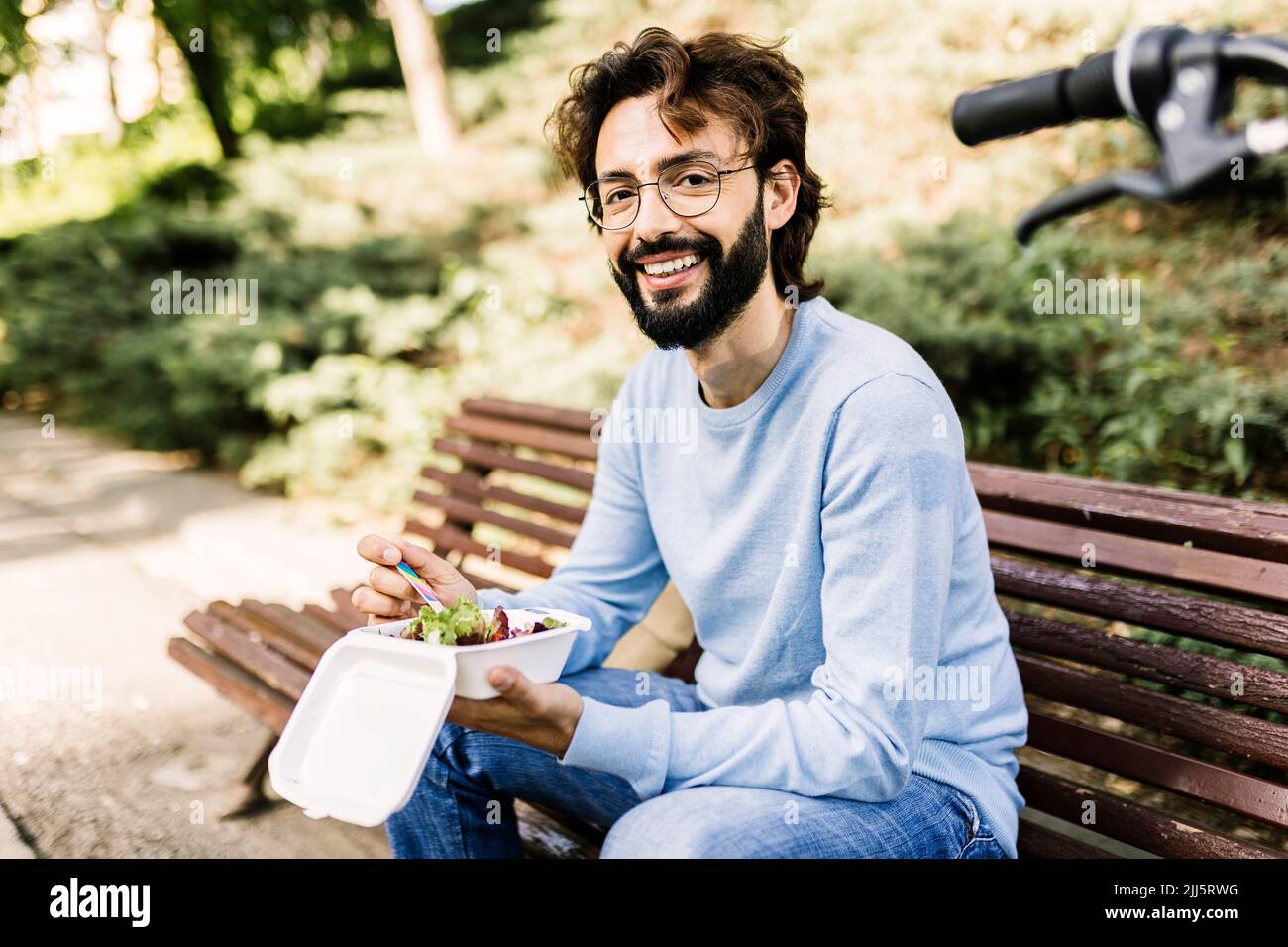 Homme heureux avec la nourriture assis sur le banc au parc Banque D'Images