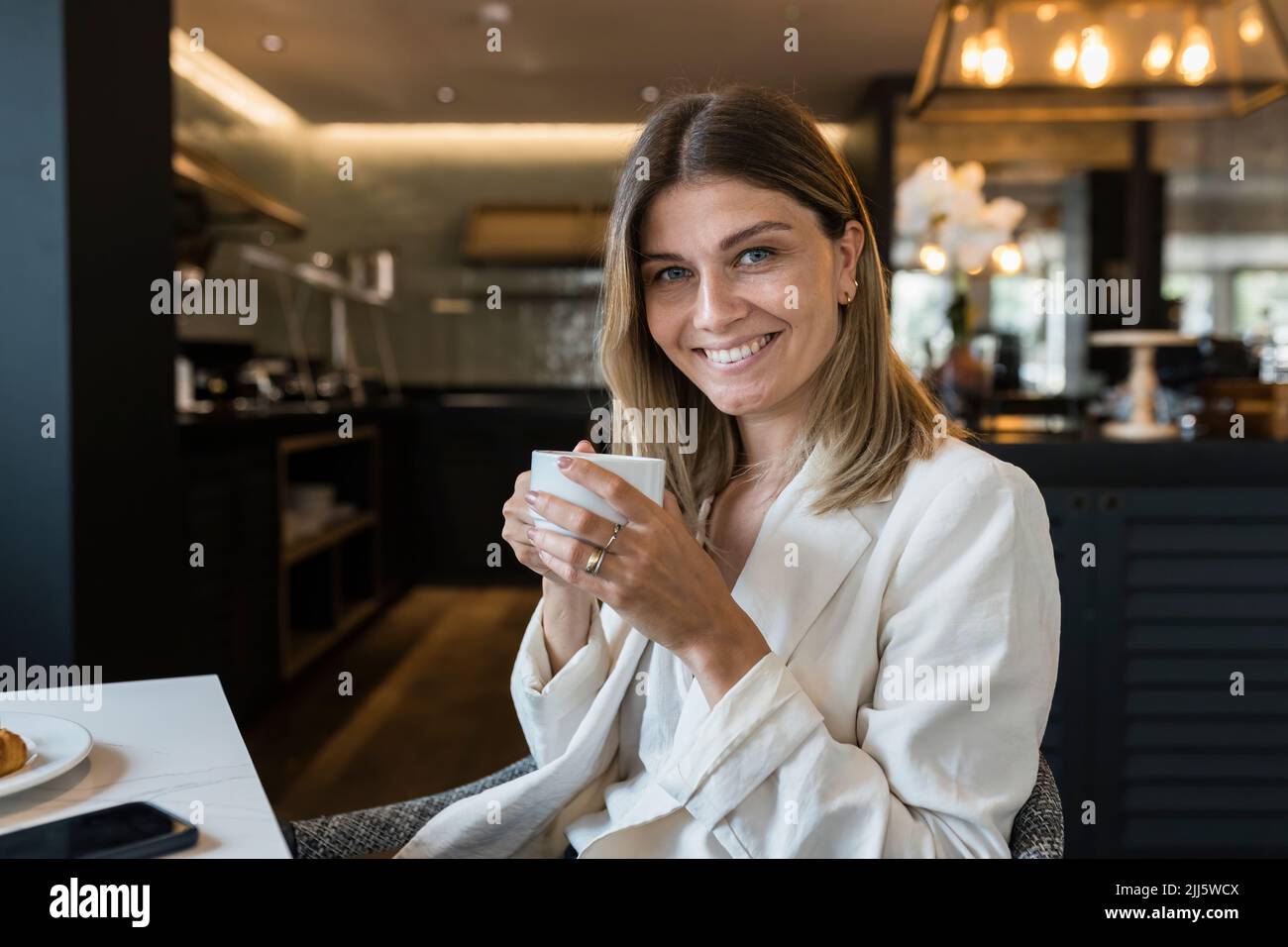 Femme d'affaires souriante tenant une tasse de café au restaurant Banque D'Images