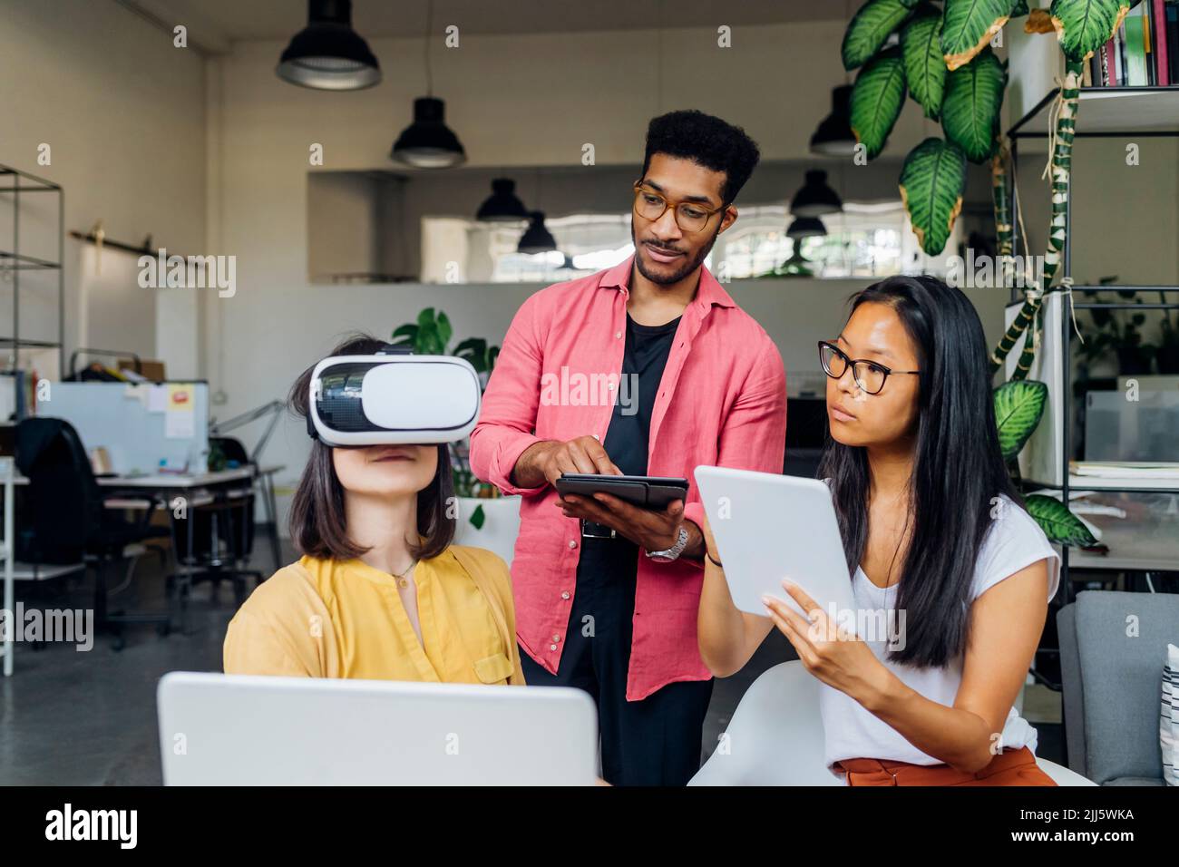 Femme d'affaires avec lunettes VR par des collègues tenant des tablettes sur le lieu de travail Banque D'Images